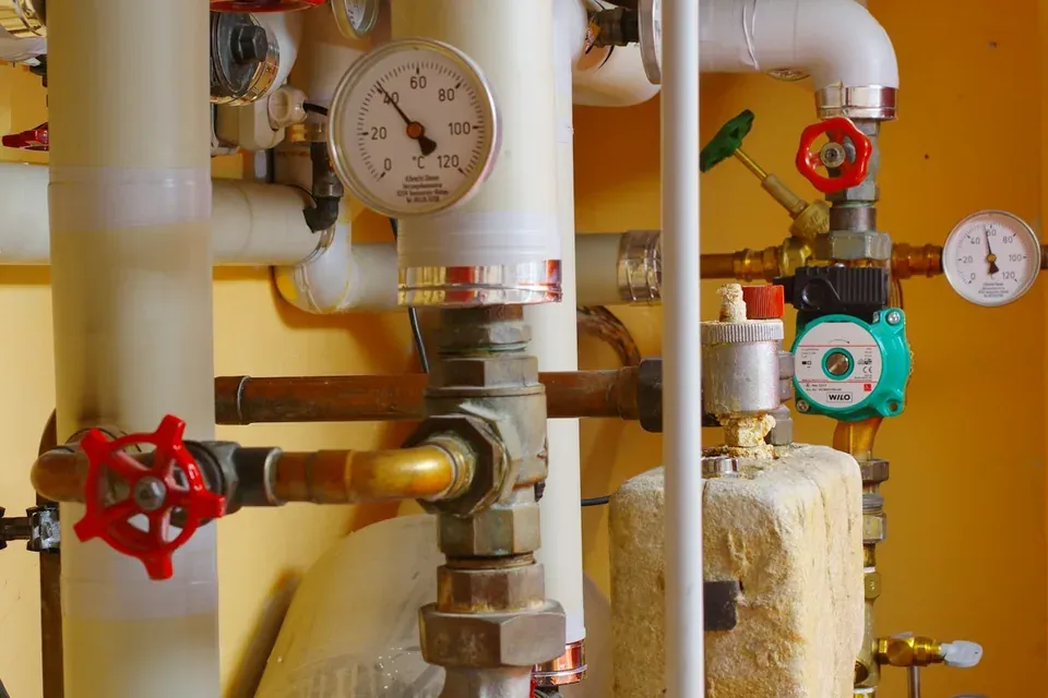 Insulated pipes, red valve wheels and a temperature gauge in a communal plant room